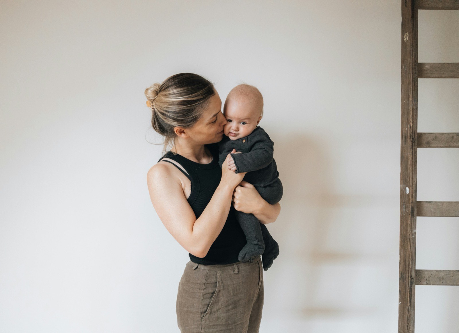 Mother kissing a baby against a cream wall